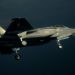 F-35 stealth fighter jet in mid-flight over the ocean with landing gear down, side view of a gray military aircraft.