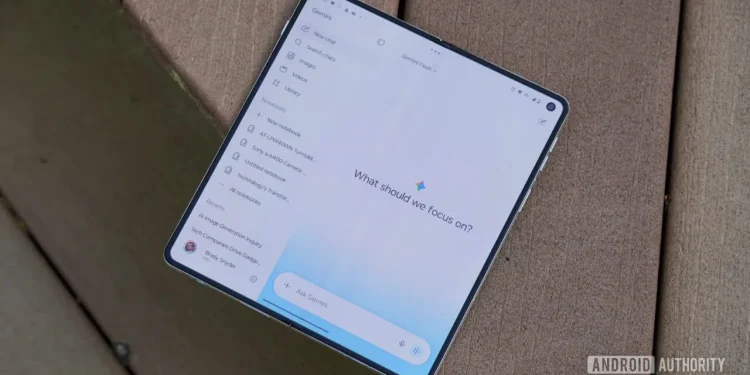 یک گوشی هوشمند تاشو (Foldable) باز شده روی سطح چوبی قرار دارد که رابط کاربری اپلیکیشن جمینای شامل منوی کناری یادداشت‌ها و عبارت «What should we focus on?» را نمایش می‌دهد