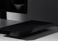 مایکروسافت Surface RTX Spark Dev Box را با قیمت 6000 دلار معرفی کرد 16 عکس تبلیغاتی با نورپردازی سینمایی از یک دستگاه کامپیوتر کوچک مشکی با بدنهی مشبکِ تهویه که روی میز سفید براق قرار گرفته و در پسزمینه، قسمت پایین یک نمایشگر روشن با تصویر مشکی محو دیده میشود. سایهی واضح دستگاه و نور موضعی، زوایای تیز و لبهی براق بدنه را برجسته میکند و کل صحنه فضایی مینیمال و تیره دارد
