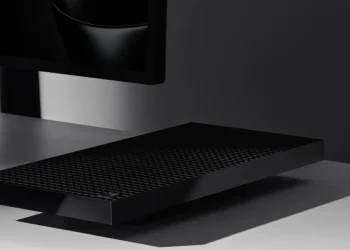 مایکروسافت Surface RTX Spark Dev Box را با قیمت 6000 دلار معرفی کرد 13 عکس تبلیغاتی با نورپردازی سینمایی از یک دستگاه کامپیوتر کوچک مشکی با بدنهی مشبکِ تهویه که روی میز سفید براق قرار گرفته و در پسزمینه، قسمت پایین یک نمایشگر روشن با تصویر مشکی محو دیده میشود. سایهی واضح دستگاه و نور موضعی، زوایای تیز و لبهی براق بدنه را برجسته میکند و کل صحنه فضایی مینیمال و تیره دارد