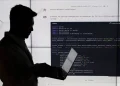 سیلوئت یک شخص در حال کار با لپ‌تاپ در برابر یک نمایشگر بزرگ که کدهای پایتون (PyTorch CNN) روی آن نمایش داده شده است.
