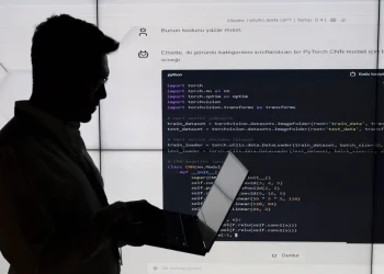 سیلوئت یک شخص در حال کار با لپ‌تاپ در برابر یک نمایشگر بزرگ که کدهای پایتون (PyTorch CNN) روی آن نمایش داده شده است.