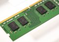 Green RAM module with a gold edge connector and black memory chips visible on a green PCB, seen at an angle.