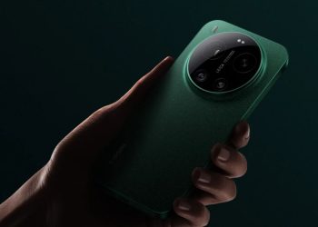 Hand holding a green smartphone with a large circular camera module on the back against a dark background, viewed from the side.