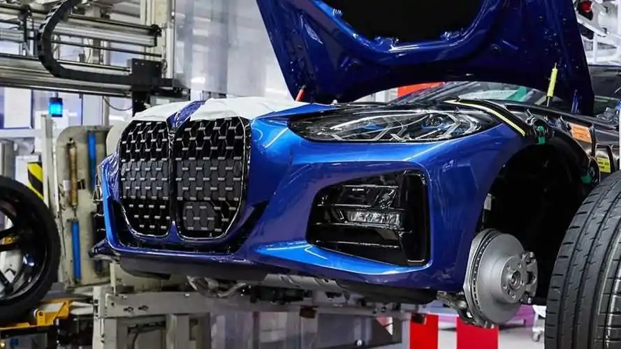 هوش مصنوعی جایگزین مدیران BMW خواهد شد 3 نمای نزدیک از قسمت جلویی یک BMW آبی در خط تولید کارخانه، با کاپوت باز و سپر جلو شامل جلوپنجره و چراغهای جلو، در میان تجهیزات کارخانه.