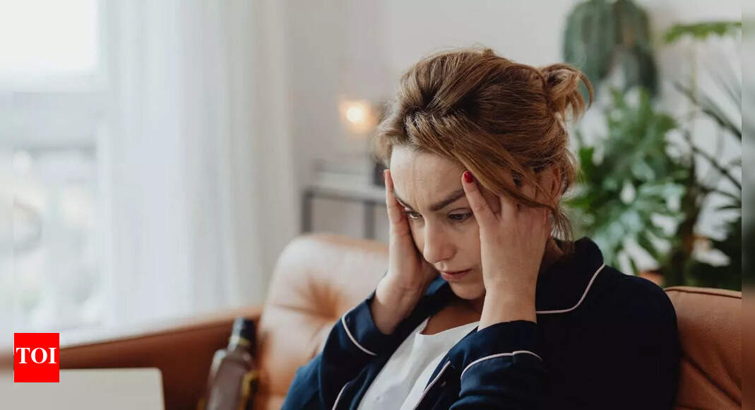 زن مضطرب روی مبل خانه می نشیند، دستانش را به شقیقه هایش فشار داده و حالتی نگران روی صورتش دارد.