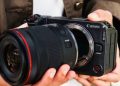 فردی دوربین بدون‌آینه Canon EOS RV را در دست گرفته و لنزی بزرگ را به بدنه آن متصل می‌کند