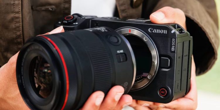 کانن نسبت به افزایش قیمت دوربین عکاسی هشدار داد 1 فردی دوربین بدونآینه Canon EOS RV را در دست گرفته و لنزی بزرگ را به بدنه آن متصل میکند