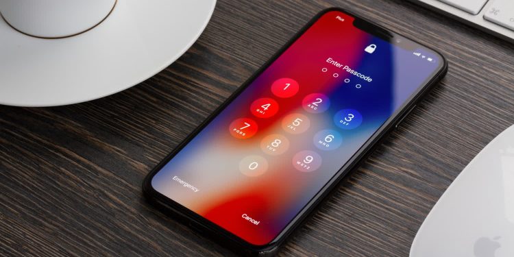 گزارش: پلیس ظاهرا یکی از امن ترین ویژگی های iOS را دور زده است 1 iPhone showing a passcode entry screen on a wooden desk with a coffee cup and keyboard nearby