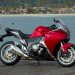 Red sport motorcycle parked on a wooden dock with a marina and boats in the background.