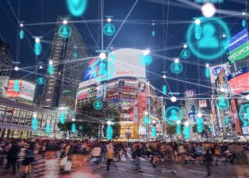 Nighttime city square with a crowded crosswalk, illuminated billboards, and teal floating user icons connected by white lines above the street, suggesting digital connectivity.